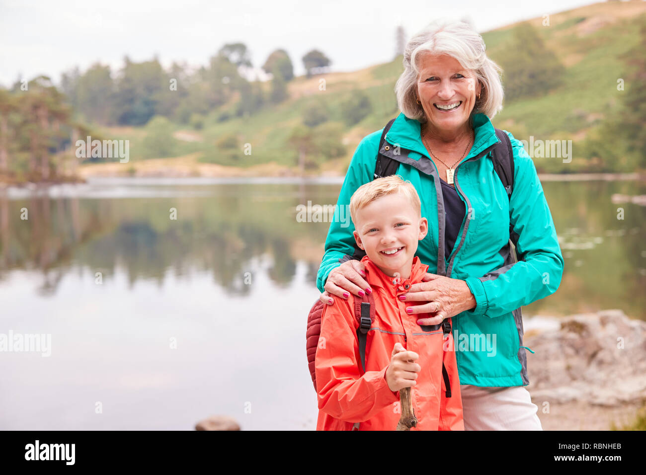 Nonna e nipote insieme in piedi vicino a un lago in campagna a sorridere alla telecamera, vicino Lake District, REGNO UNITO Foto Stock