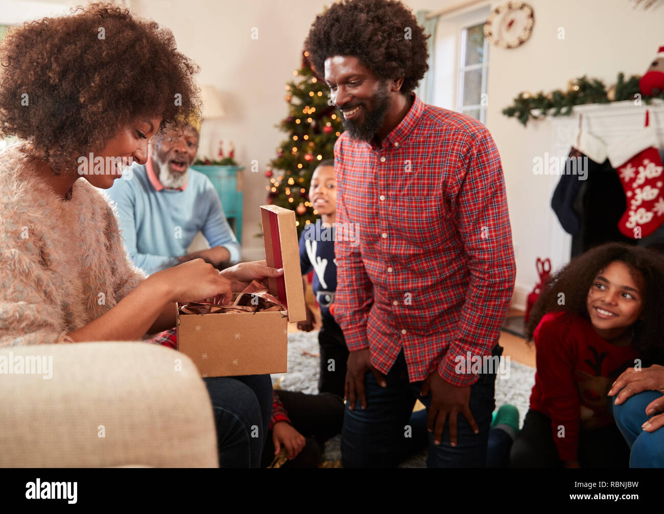 Giovane lo scambio di doni come Multi generazione Famiglia festeggiano il Natale a casa insieme Foto Stock