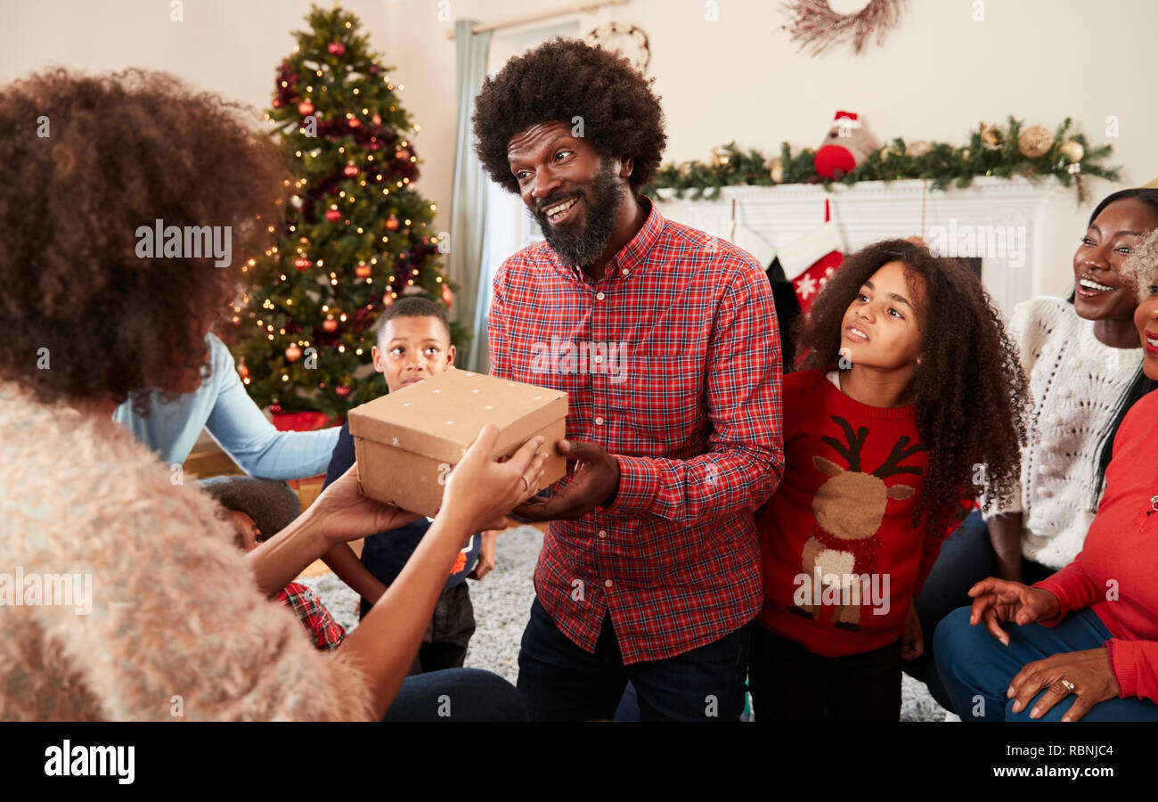 Giovane lo scambio di doni come Multi generazione Famiglia festeggiano il Natale a casa insieme Foto Stock