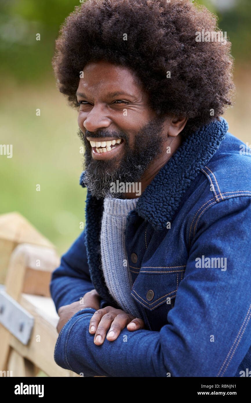 Uomo nero appoggiato su di una recinzione di legno in campagna a ridere, close up Foto Stock