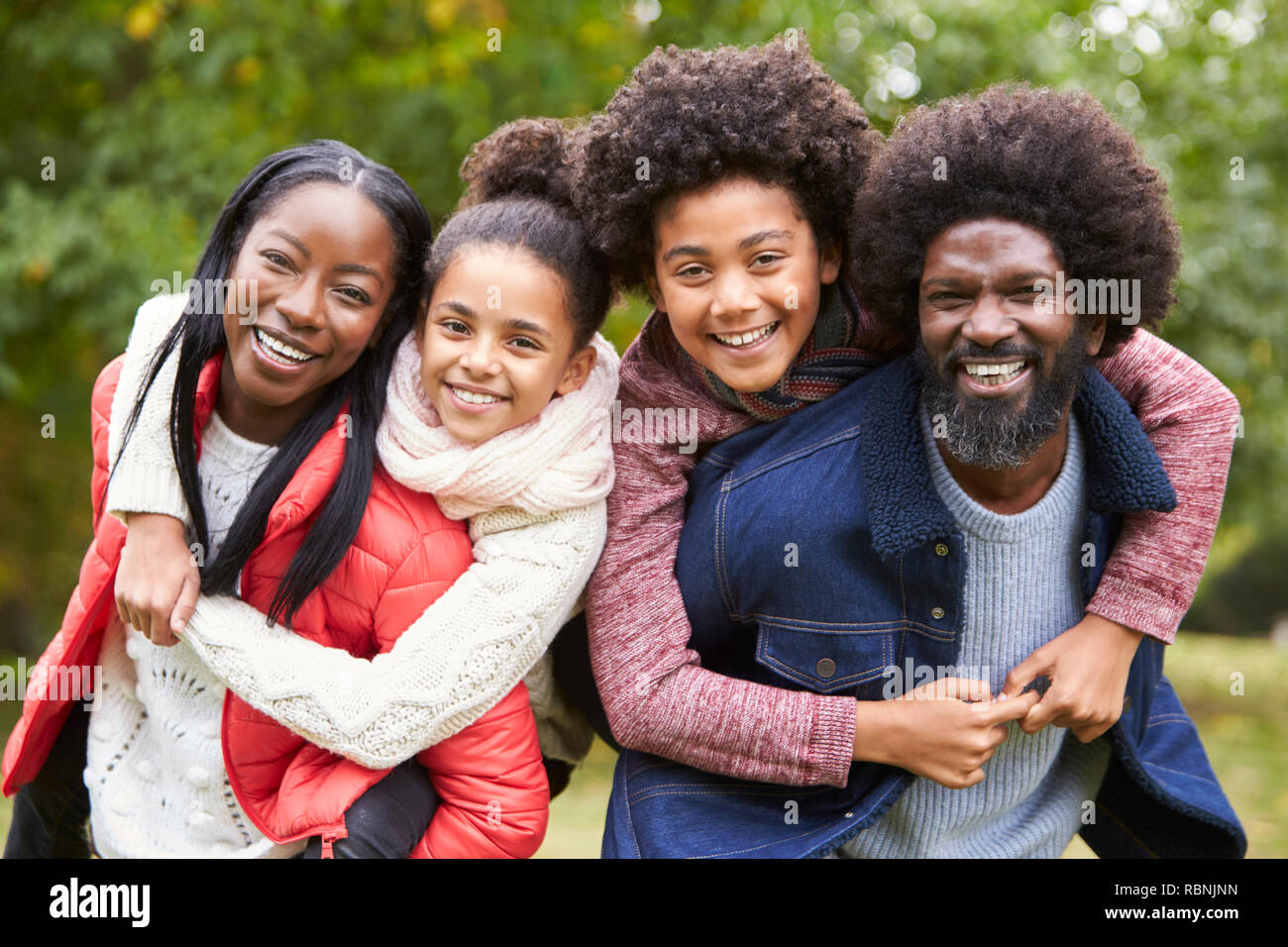 Razza mista famiglia sorridente alla telecamera, genitori piggybacking kids in campagna, vicino fino Foto Stock