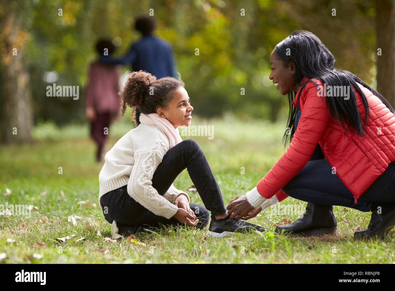 Giovane donna nera aiutando a sua figlia di legare le sue scarpe durante una bella passeggiata in famiglia nel parco, angolo basso Foto Stock