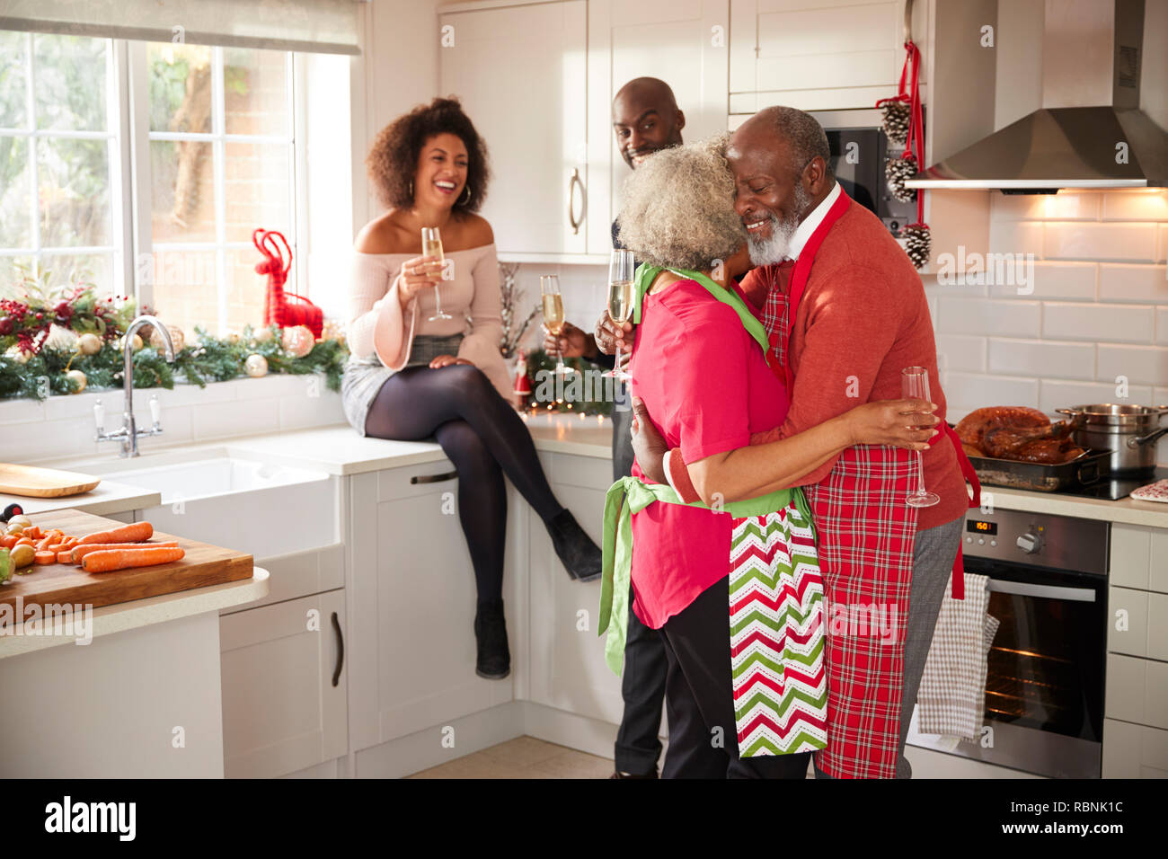 Multi-etnico famiglia adulto celebrando con champagne, parlare e ballare in cucina mentre si prepara la cena il giorno di Natale Foto Stock