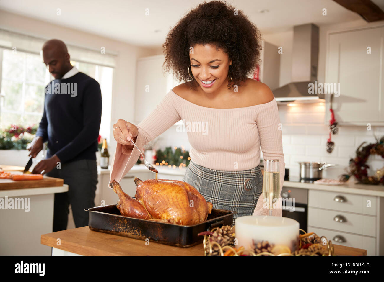 I giovani adulti razza mista giovane preparare la cena di Natale insieme a casa, donna inumidendo il tacchino arrosto in primo piano, vista frontale, close up Foto Stock