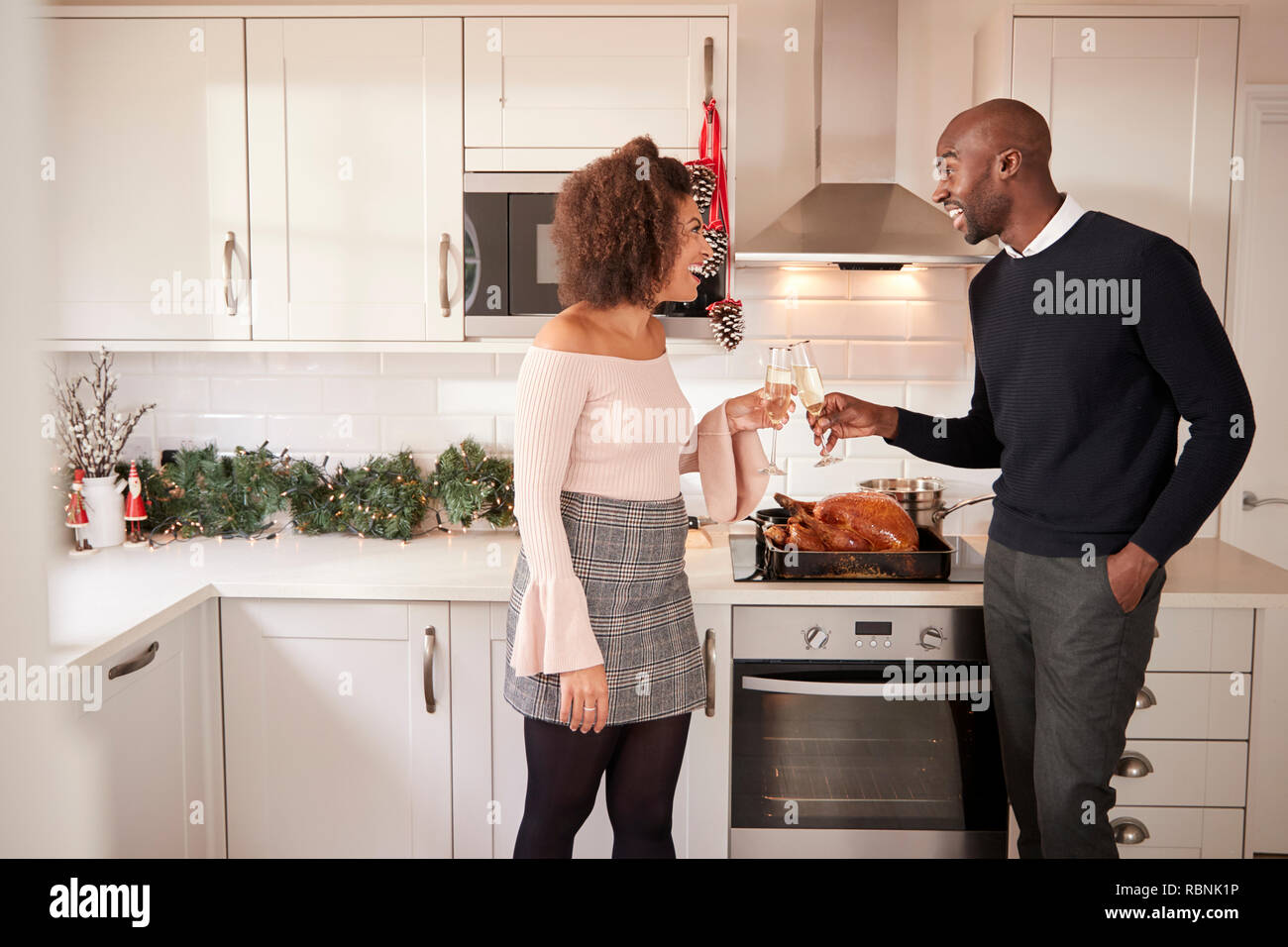 I giovani adulti razza mista giovane fare un brindisi con champagne nella loro cucina mentre prepara la cena di Natale, vista laterale Foto Stock