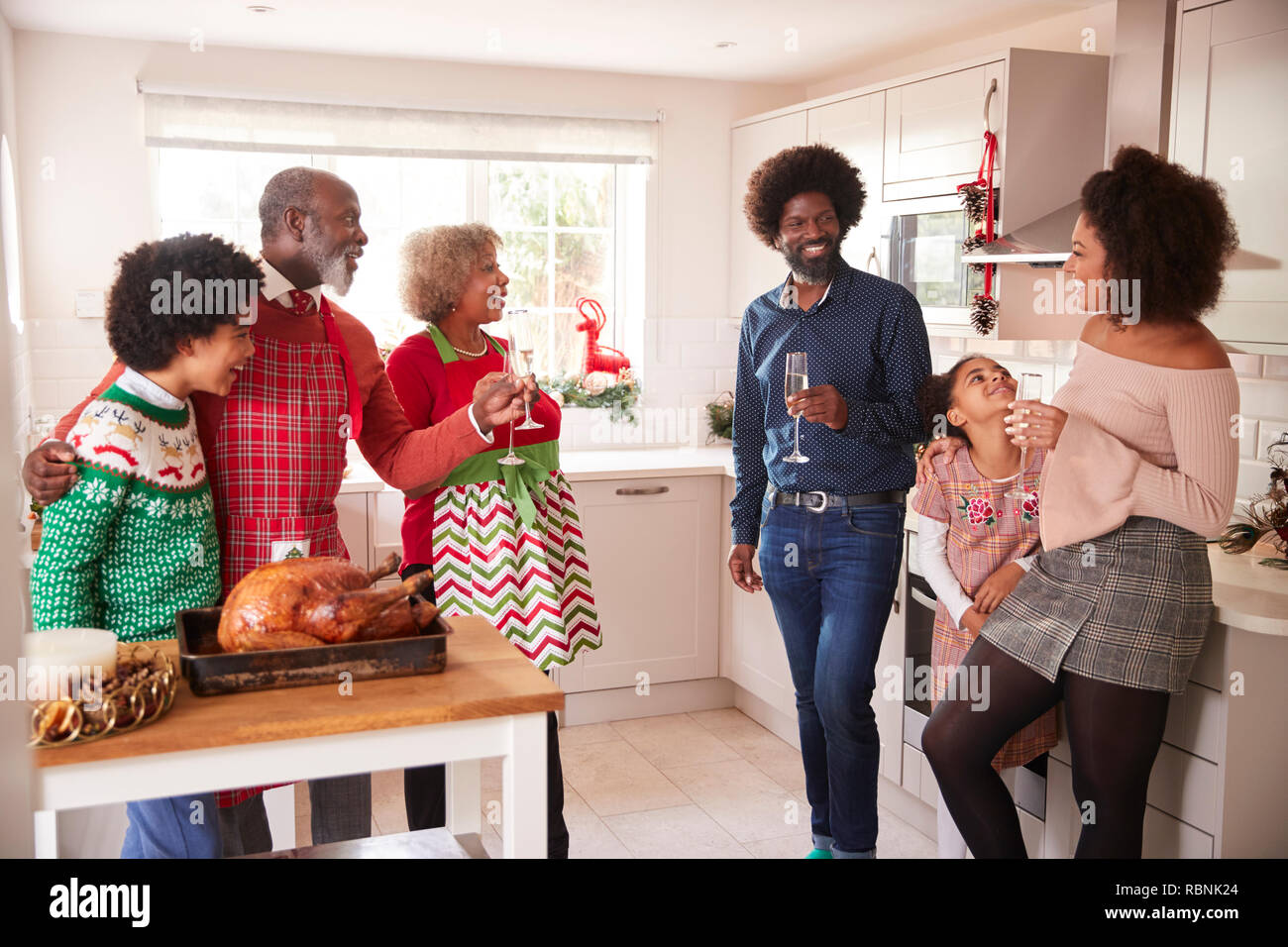 Razza mista, multi generazione parla di famiglia e di bere champagne in cucina mentre si prepara la cena di Natale insieme Foto Stock