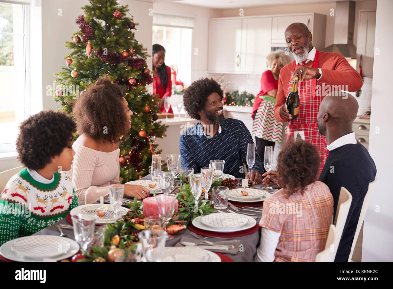 Nonno nero apertura champagne per la sua generazione multi family, riuniti nella sala da pranzo per la cena di Natale Foto Stock