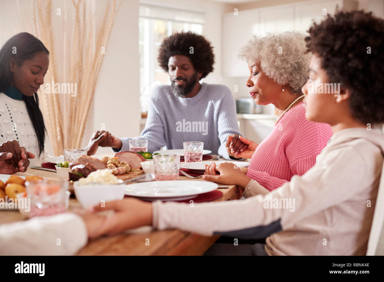 Generazione Multi razza mista famiglia tenendo le mani e dicendo la grazia prima di mangiare la loro cena di domenica, il fuoco selettivo Foto Stock