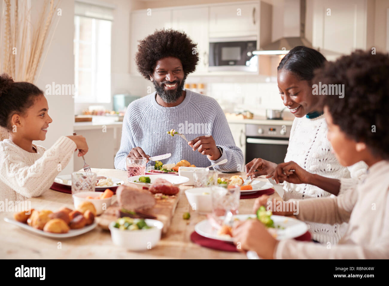 Felice razza mista giovane famiglia di quattro di mangiare la domenica a cena insieme, vista frontale Foto Stock