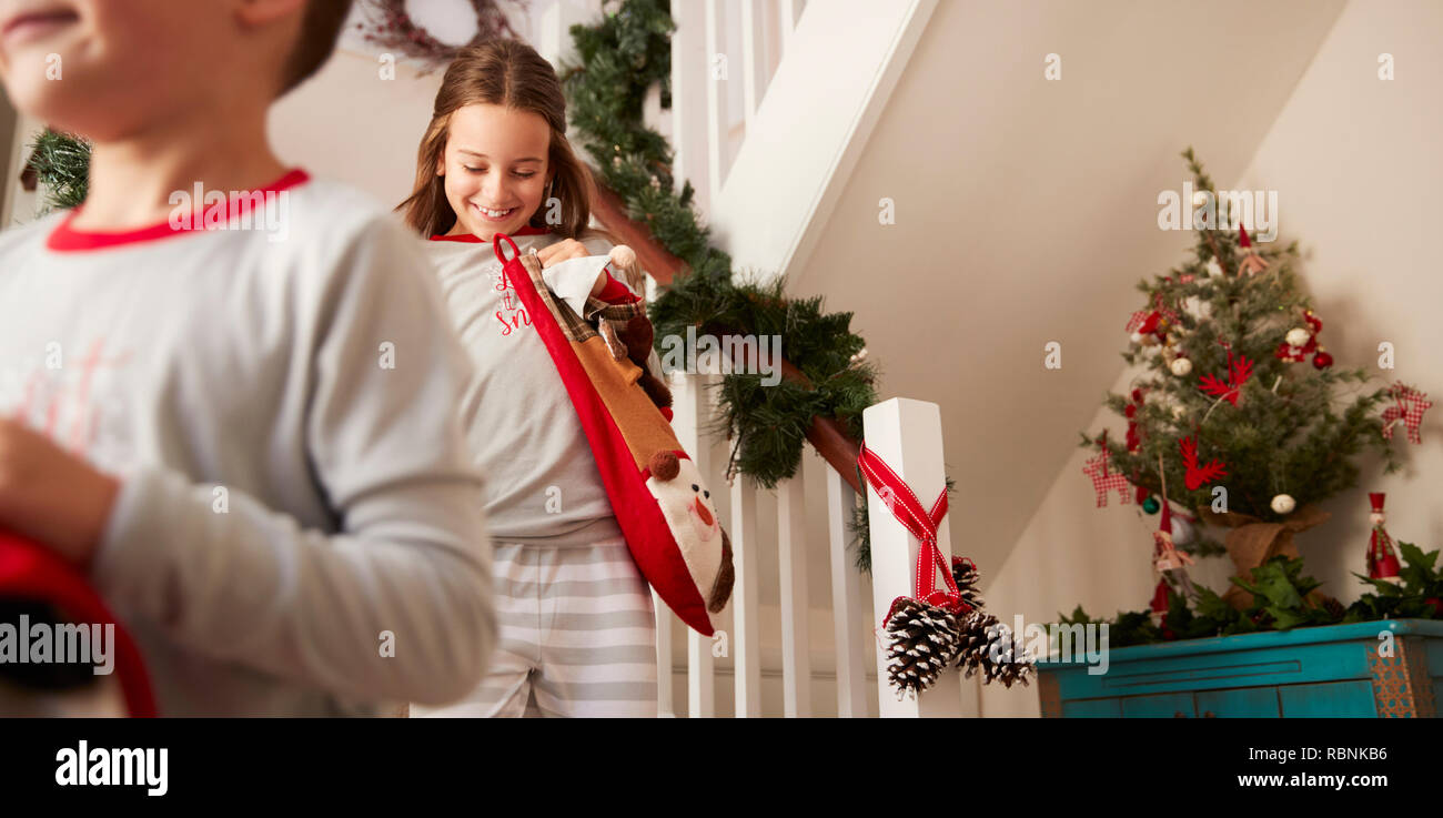 Due bambini eccitati indossando pigiami correndo giù per le scale tenendo le calze sulla mattina di Natale Foto Stock