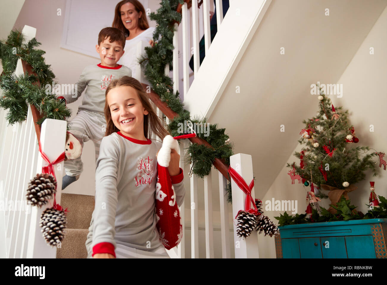 Famiglia eccitato indossando pigiami correndo giù per le scale tenendo le calze sulla mattina di Natale Foto Stock