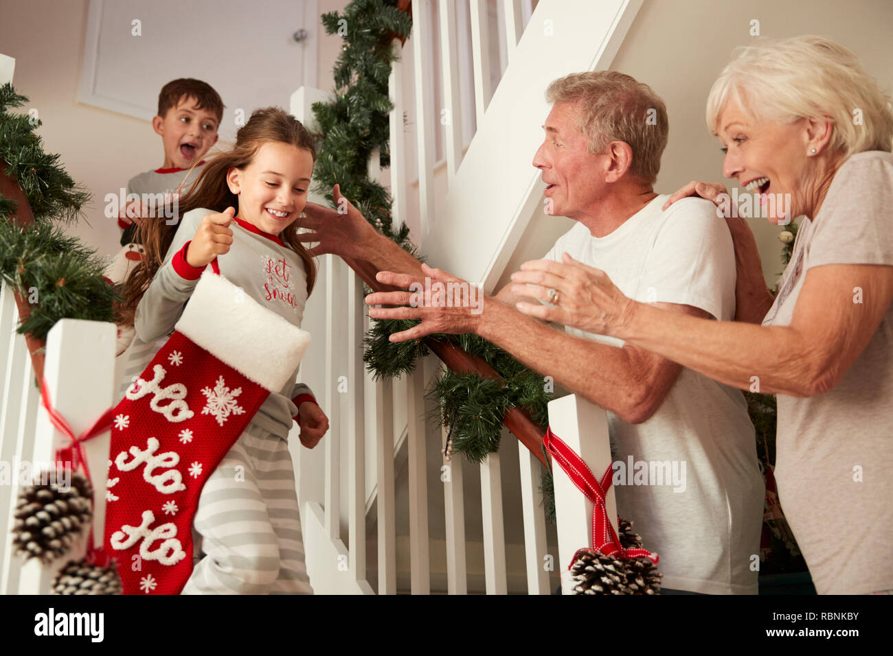 Saluto i nonni entusiasti nipoti indossando pigiami correndo giù per le scale tenendo le calze sulla mattina di Natale Foto Stock