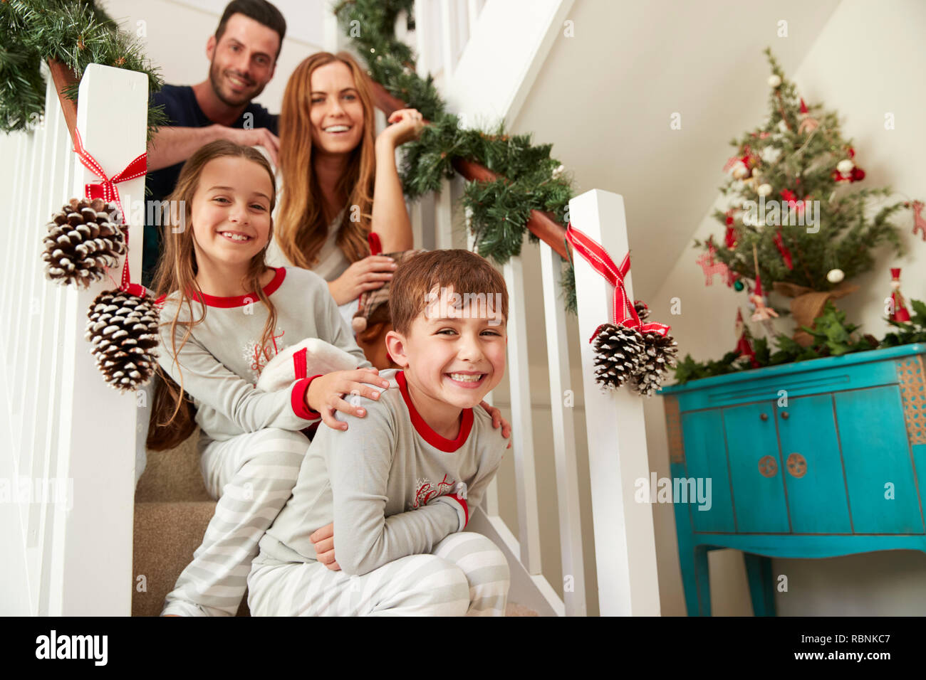 Ritratto di famiglia eccitato indossando pigiami seduti sulle scale la mattina di Natale Foto Stock