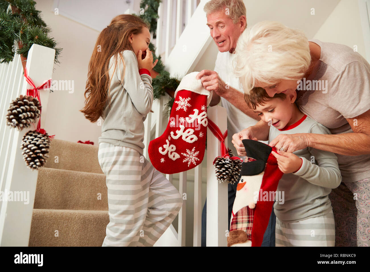 Saluto i nonni entusiasti nipoti indossando pigiami correndo giù per le scale tenendo le calze sulla mattina di Natale Foto Stock