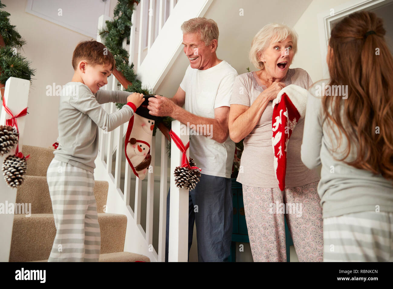 Saluto i nonni entusiasti nipoti indossando pigiami correndo giù per le scale tenendo le calze sulla mattina di Natale Foto Stock