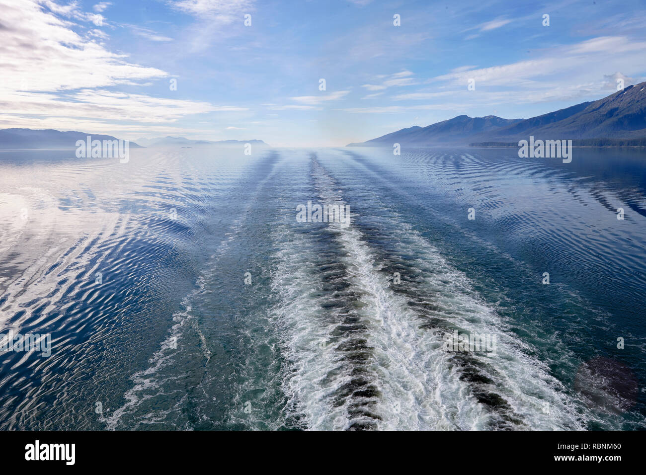 Scia della barca sul lago in Alaska circondato da montagne e foreste Foto Stock