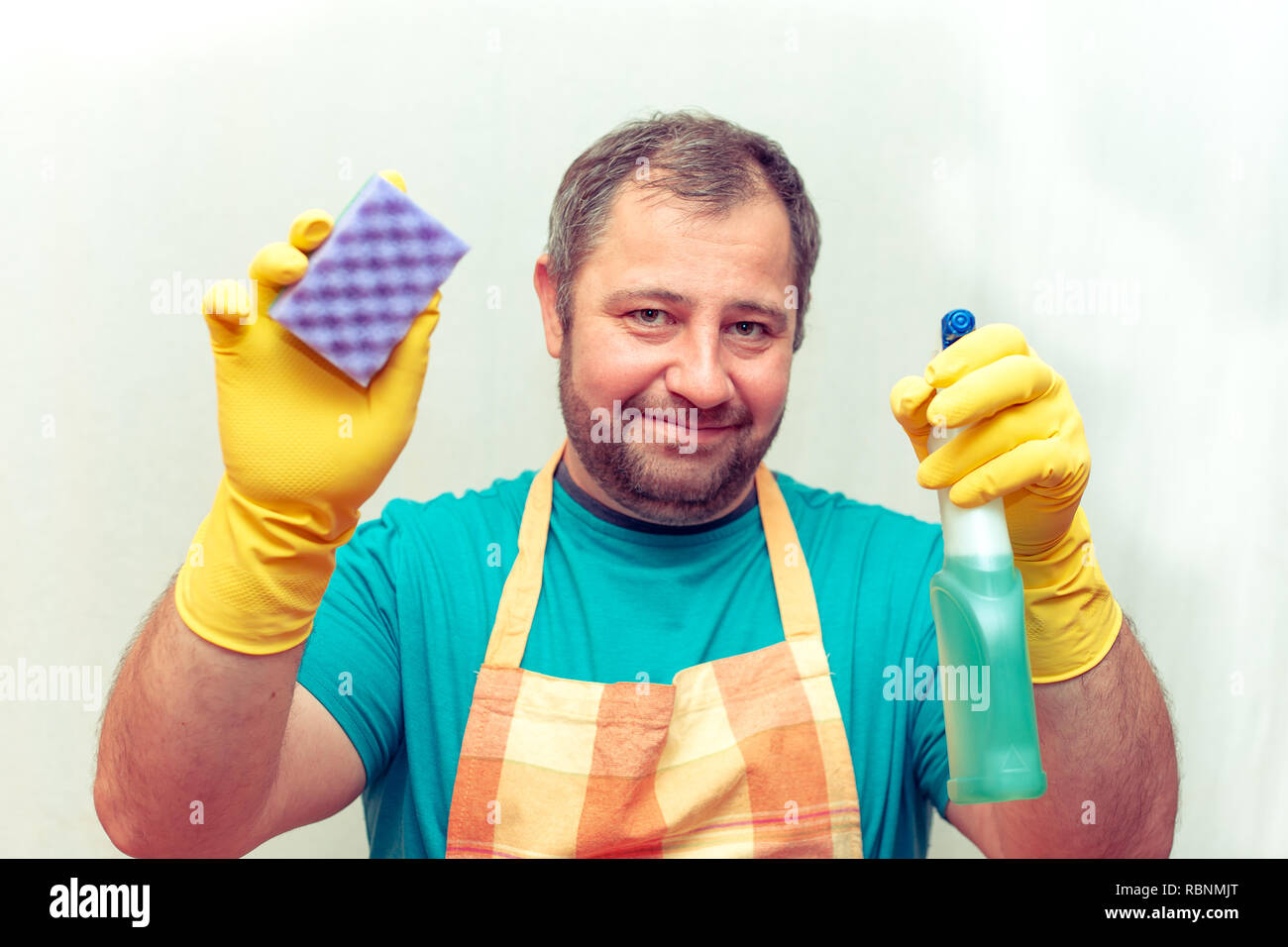 Emotivo uomo barbuto tenendo una spugna e un agente di pulizia. Sfondo bianco Foto Stock