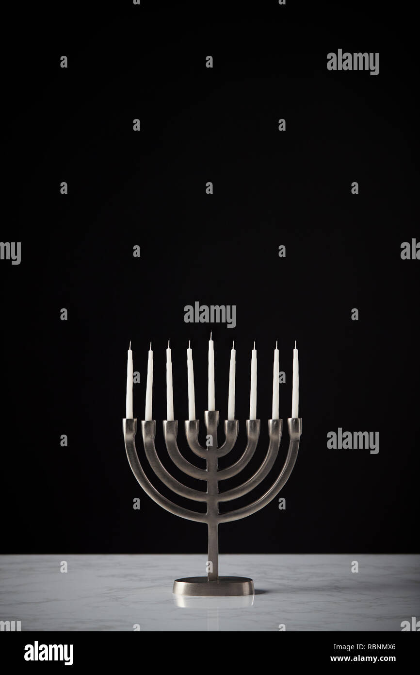 Metallo Hanukkah Menorah con candele non illuminata sulla superficie di marmo contro il nero di sfondo per studio Foto Stock