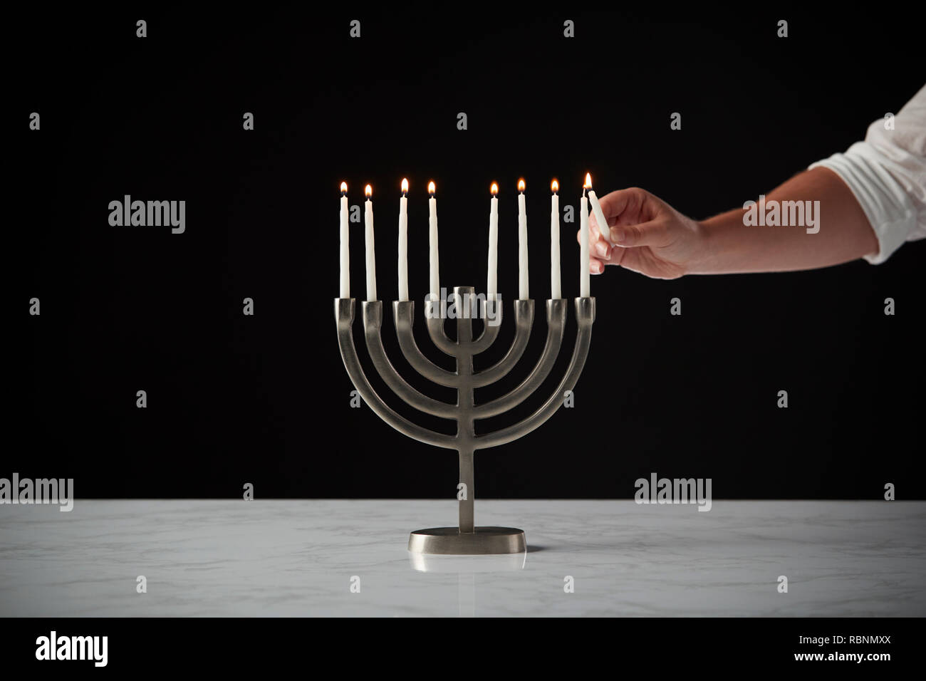 Illuminazione a mano candela su metallo Hanukkah Menorah sulla superficie di marmo contro il nero di sfondo per studio Foto Stock
