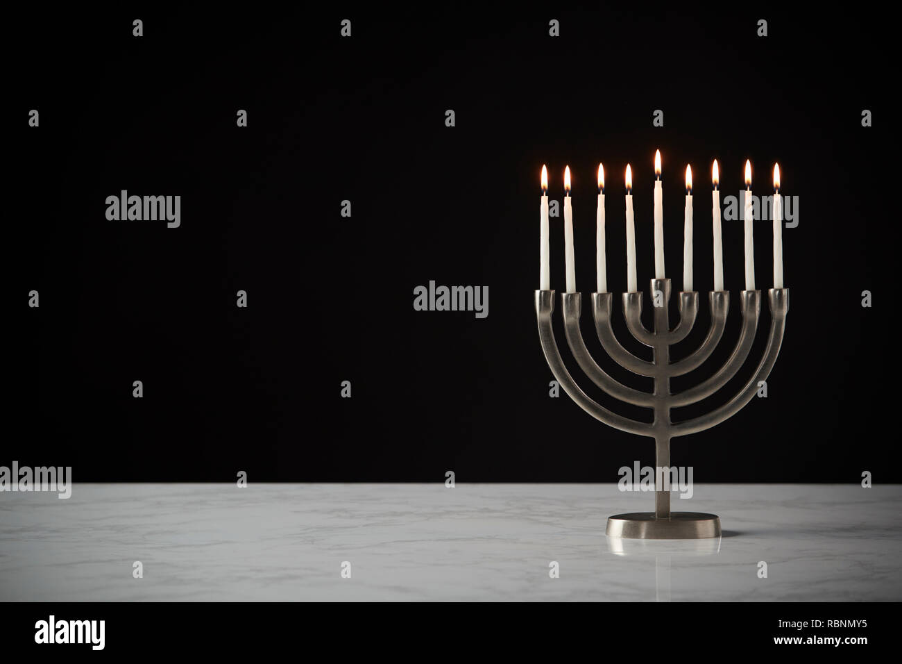 Candele accese sul metallo Hanukkah Menorah sulla superficie di marmo contro il nero di sfondo per studio Foto Stock