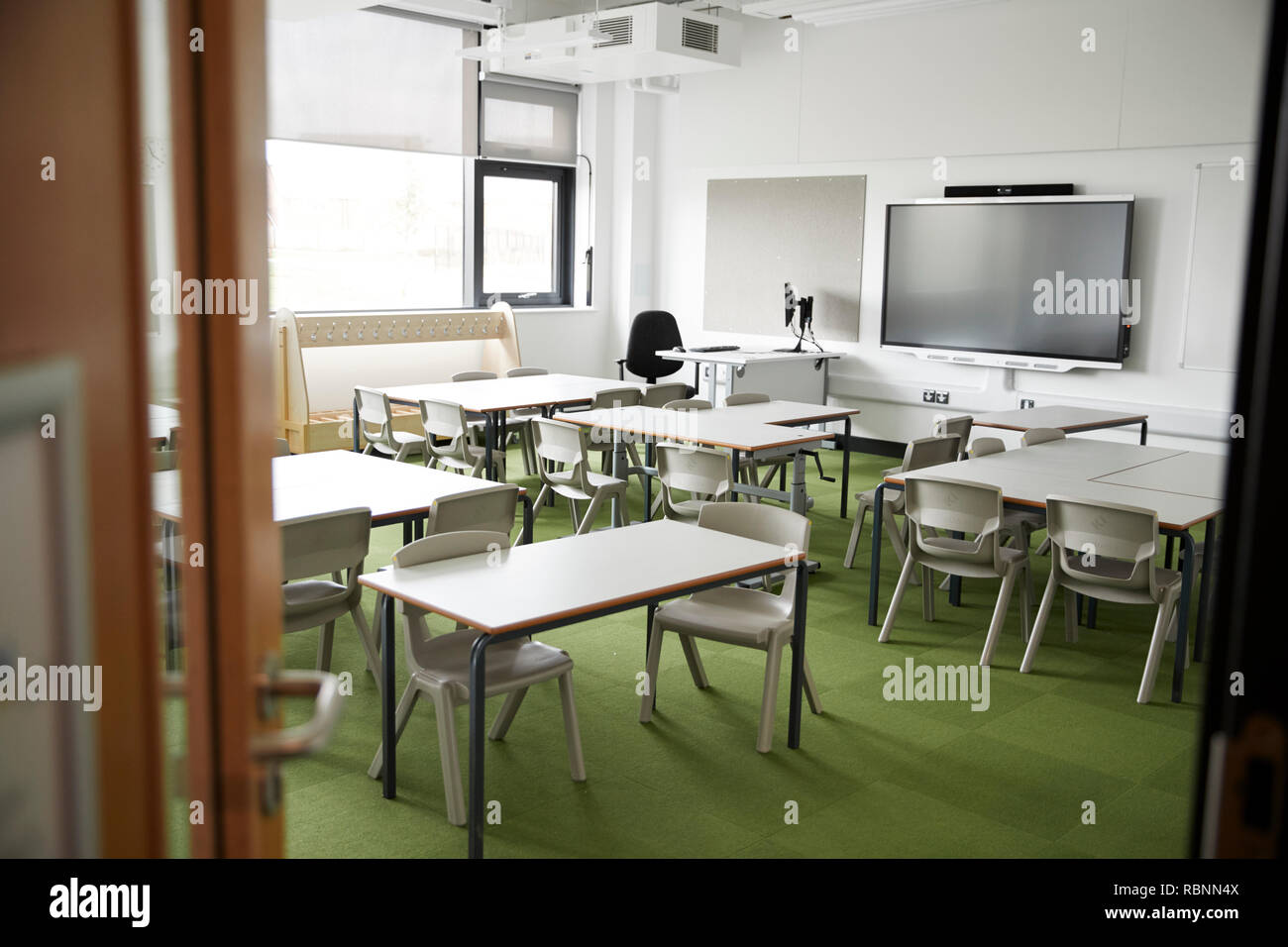 Un aula vuota in una scuola primaria con il bianco scrivanie e sedie, visto dalla porta Foto Stock