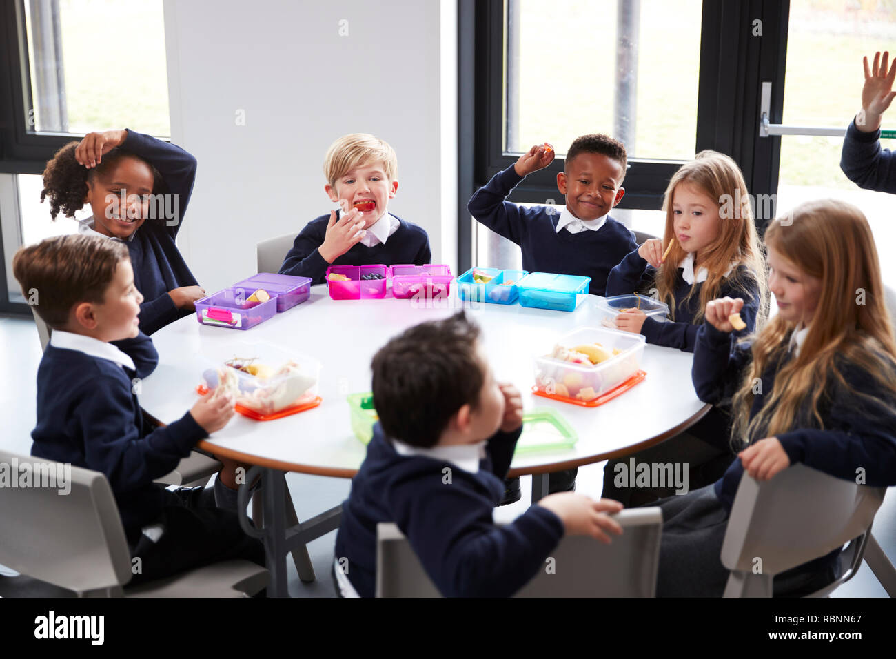 Vista in elevazione della scuola primaria i bambini seduti insieme attorno ad una tavola rotonda di mangiare il loro pranzo al sacco Foto Stock