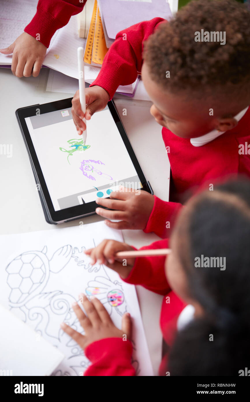 Vista in elevazione di due kindergarten scuola i bambini seduti ad una scrivania in un disegno in aula con un computer tablet e stilo, close up, verticale Foto Stock