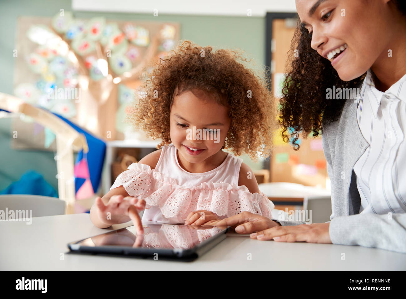Giovani razza mista schoolgirl utilizzando un computer tablet con un neonato femmina insegnante di scuola, lavorando su un insieme in una classe, close up Foto Stock