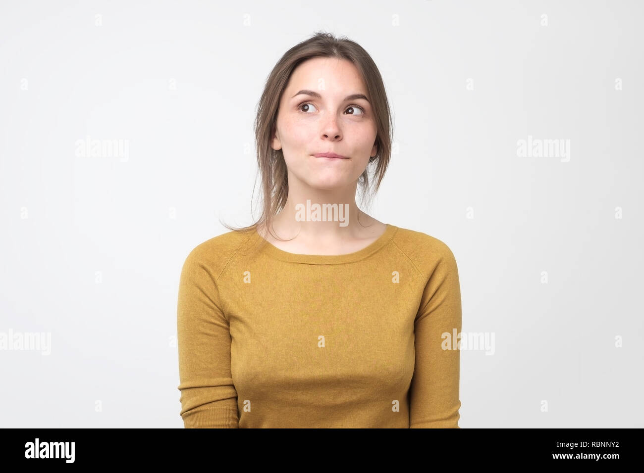 Giovane donna difficile avere qualcosa in mente con sly espressioni facciali, su sfondo grigio Foto Stock