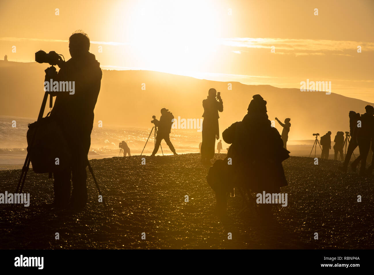 Sagome di fotografi in spiaggia al tramonto nella luce dorata Foto Stock