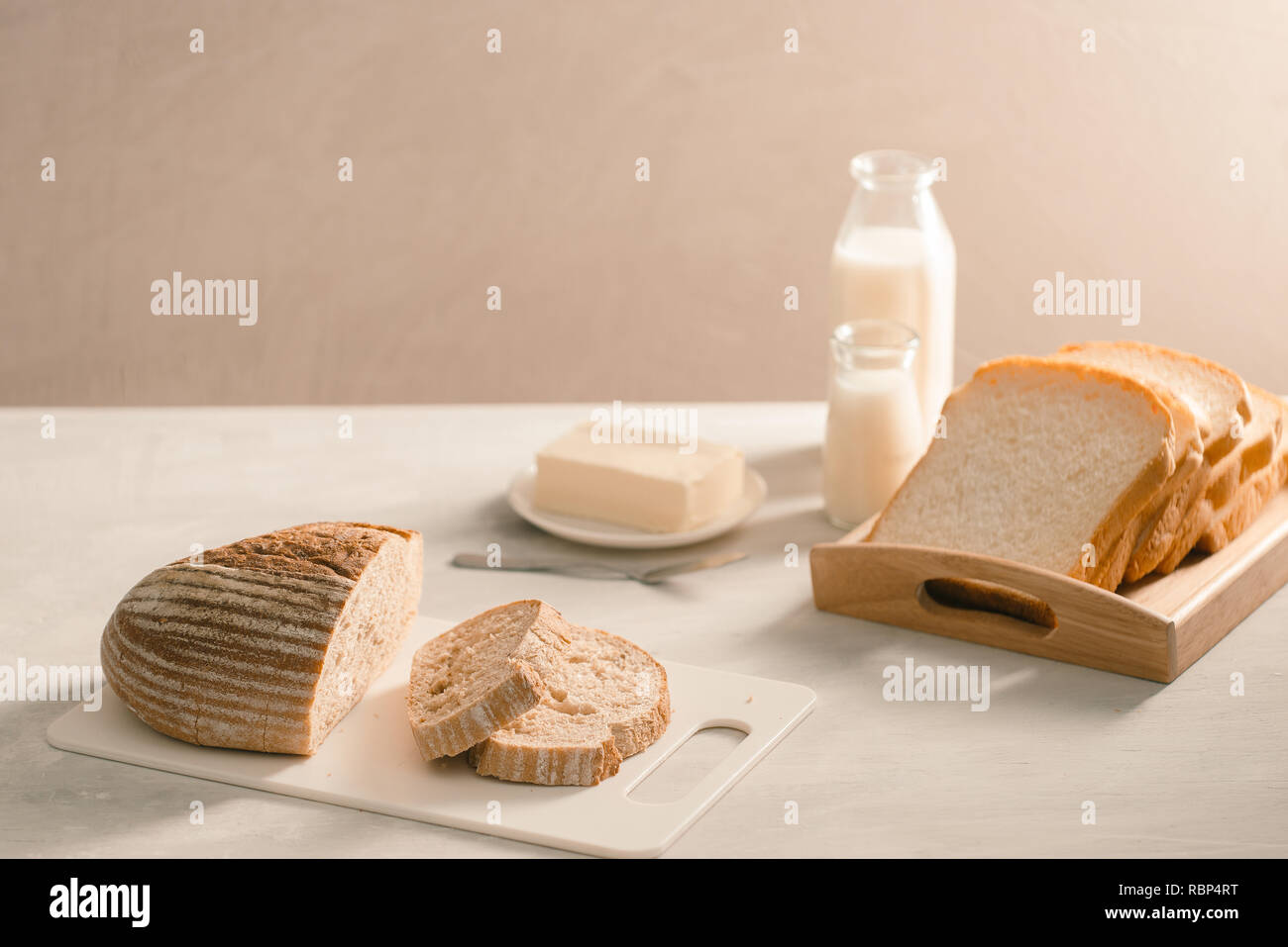 Pane sulla piastra di supporto circondato da burro e latte sul tavolo bianco close-up Foto Stock