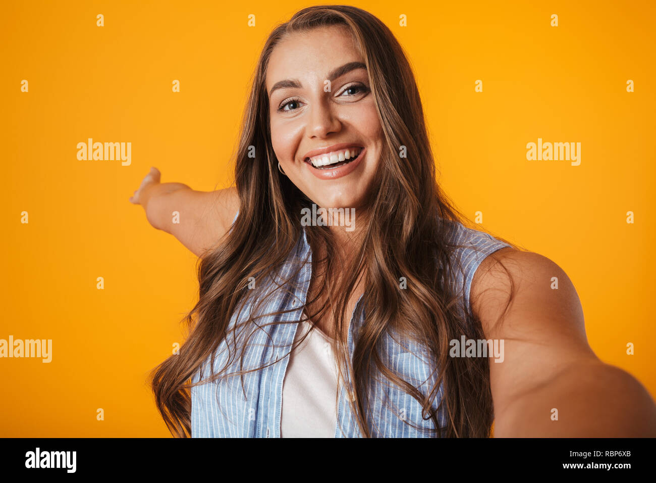 Allegro sovrappeso giovane donna in piedi isolato su sfondo giallo, prendendo un selfie Foto Stock