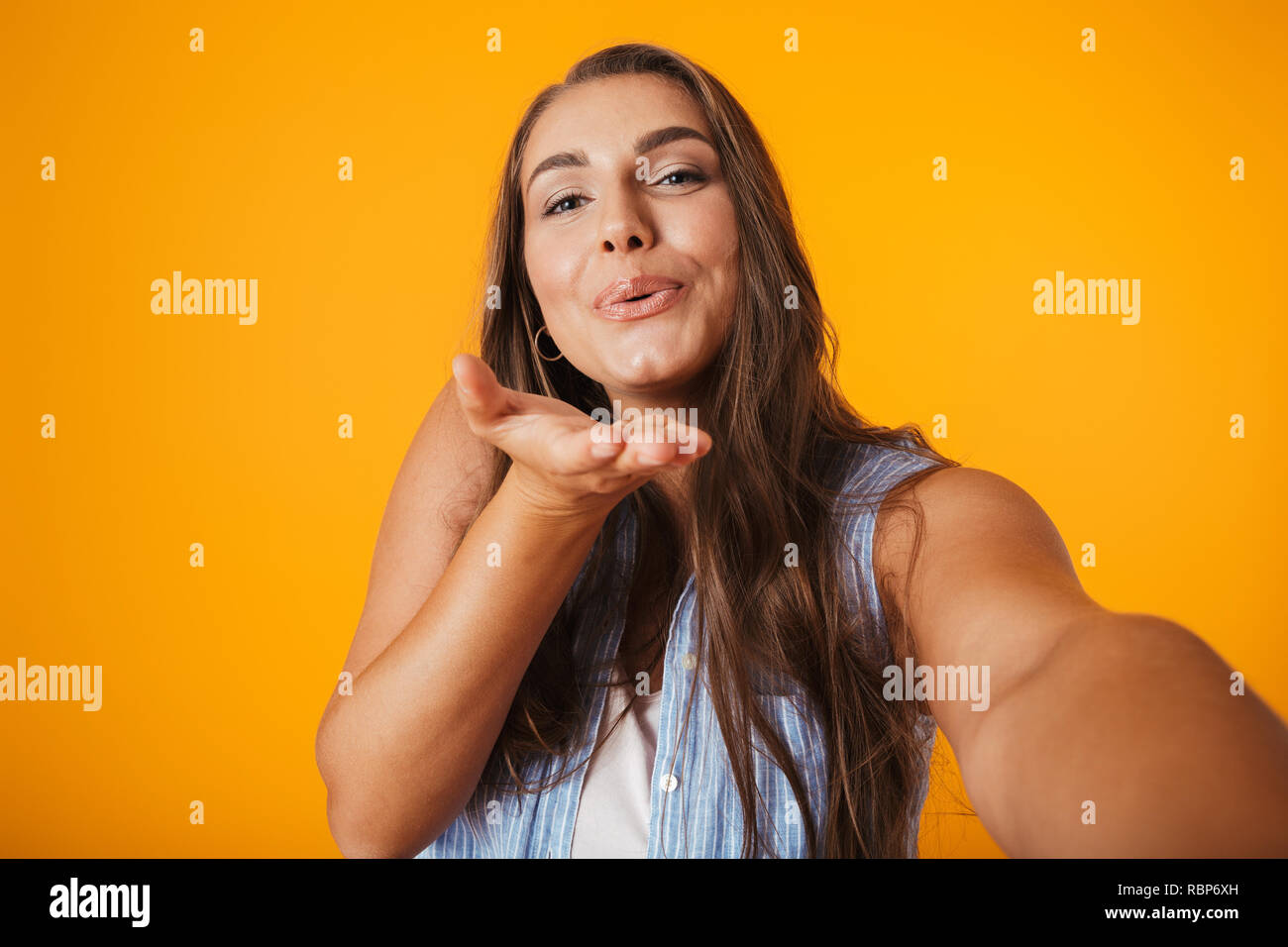 Allegro sovrappeso giovane donna in piedi isolato su sfondo giallo, prendendo un selfie Foto Stock