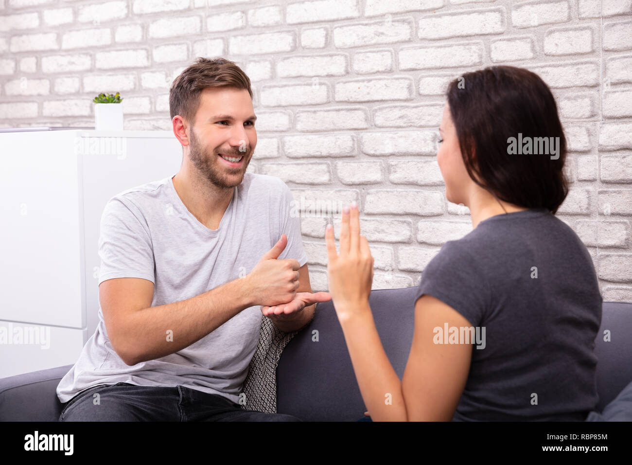 Sorridente Coppia giovane seduto sul divano comunicante con la lingua dei segni Foto Stock