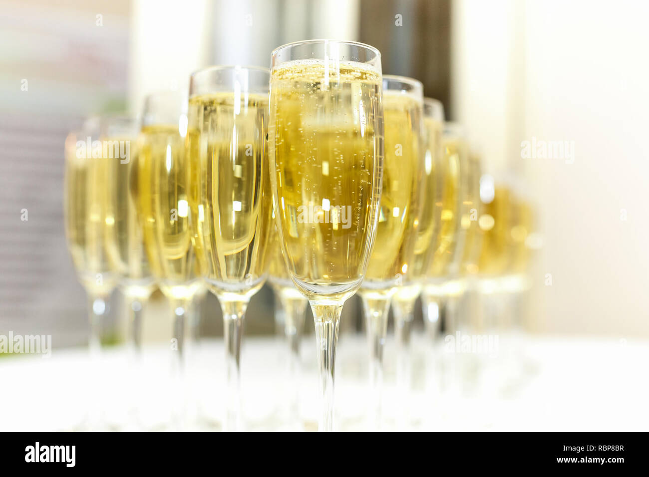 Sacco di offuscata occhiali con champagne sulla ricezione delle parti tabella su sfondo chiaro Foto Stock