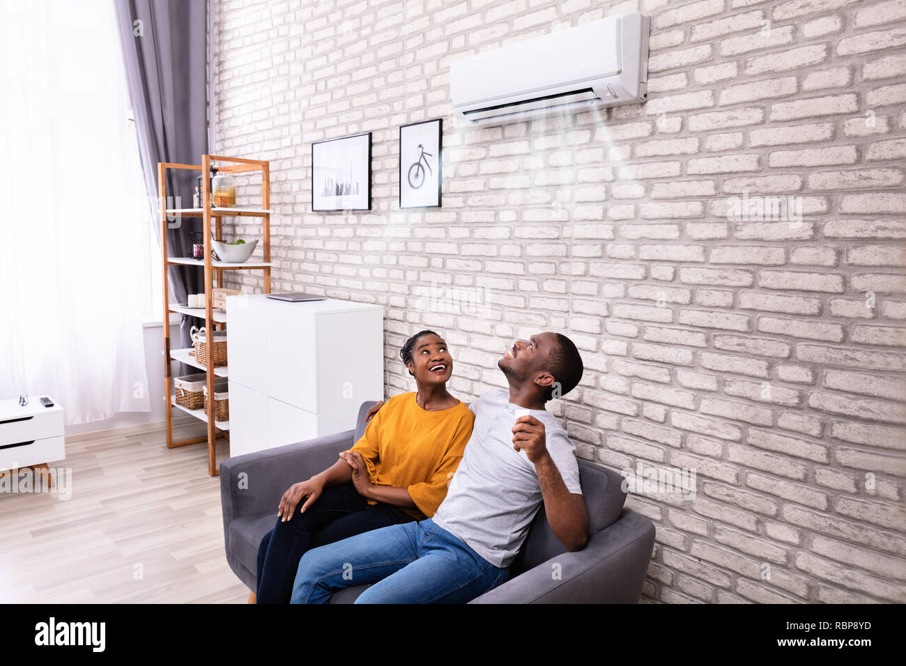 Giovane africano giovane seduto sul divano di funzionamento del condizionatore d'aria di casa Foto Stock