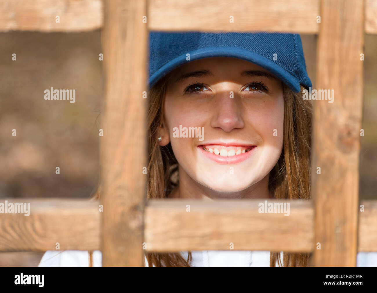 Una giovane ragazza che indossa una sfera blu cappuccio sorrisi a fotocamera da behine un latice in legno. Foto Stock