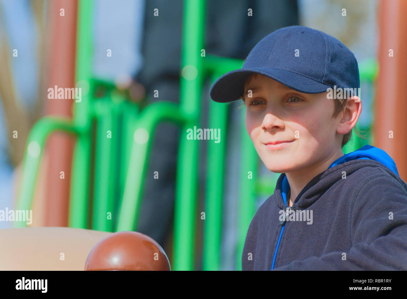 Un giovane ragazzo in un parco giochi in una giornata di sole indossare una sfera blu cap. Foto Stock