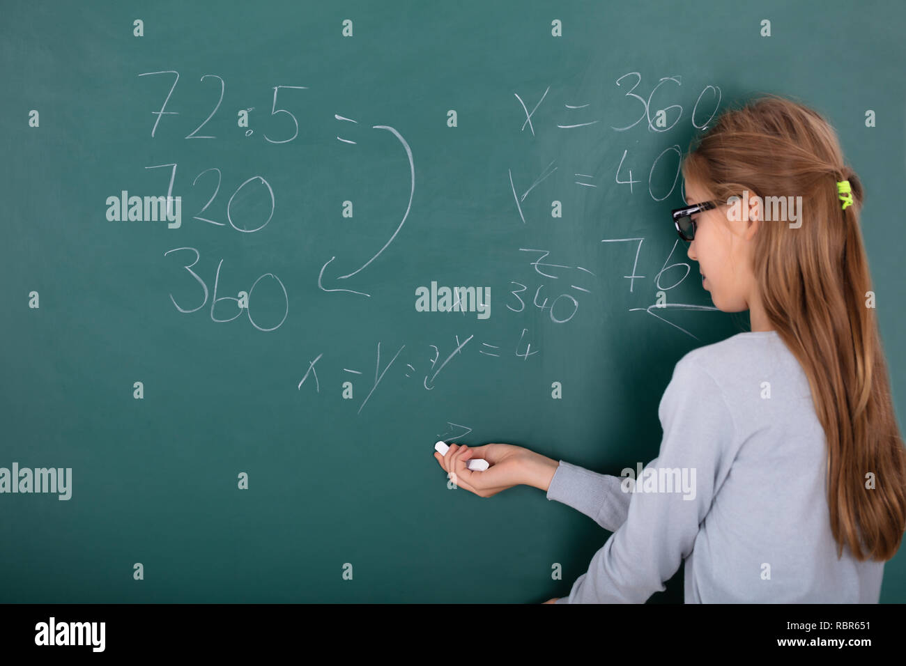 Vista posteriore di una ragazza che indossa occhiali risolvere la matematica sulla lavagna Foto Stock