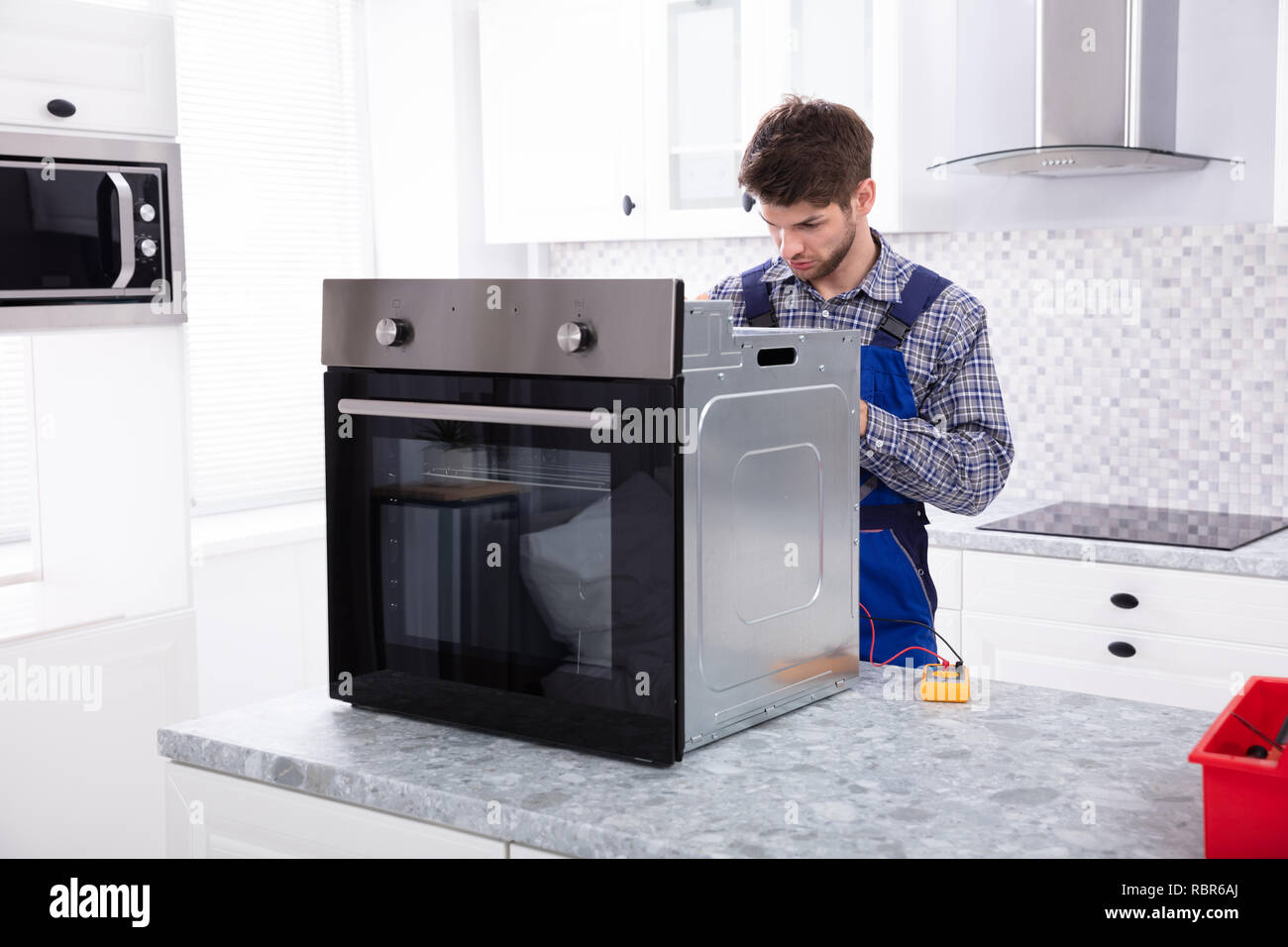 Giovane Maschio Repairman Riparazione di forno usando un multimetro digitale in cucina Foto Stock