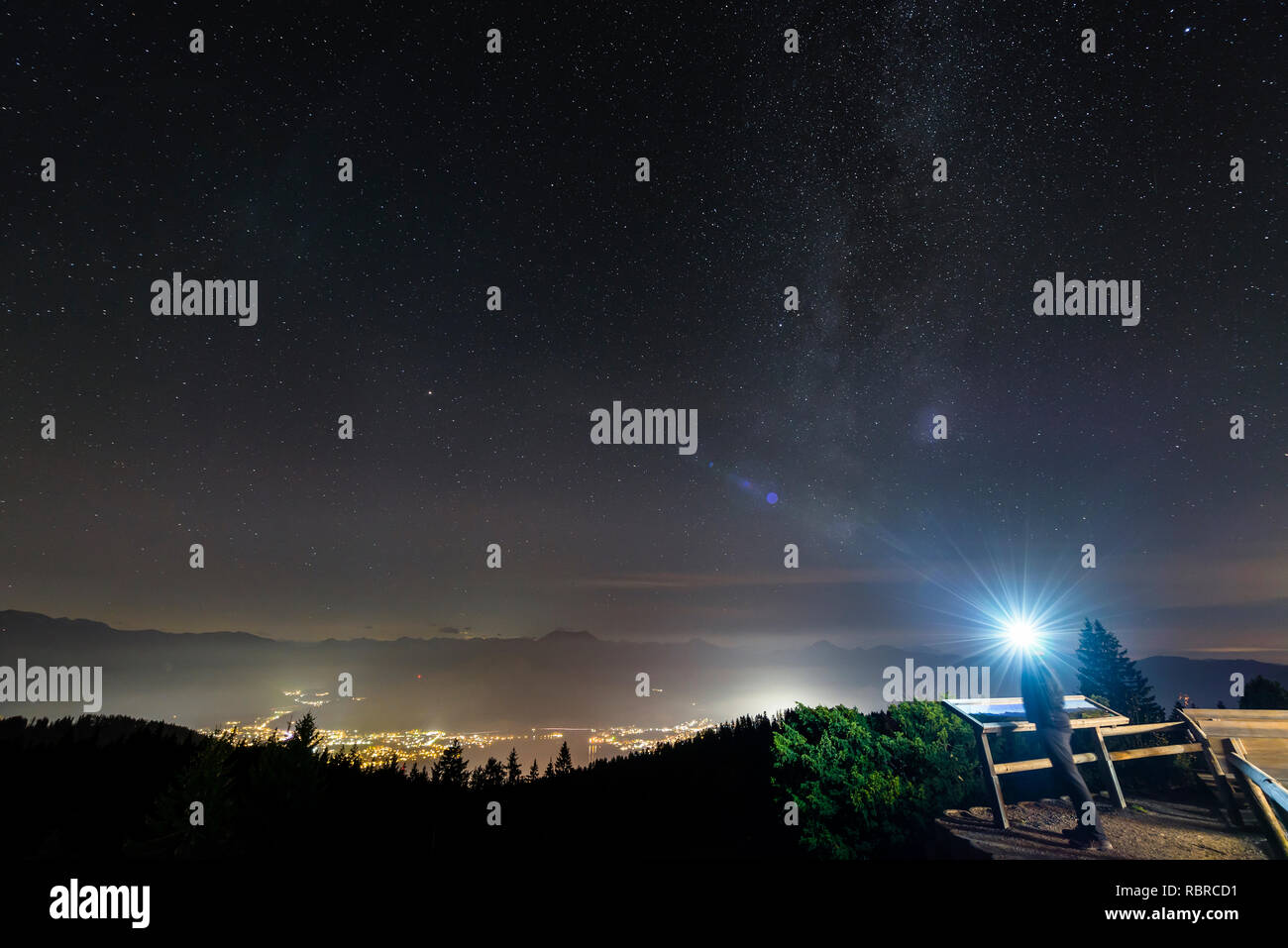 Uomo con proiettore luminoso guarda il cielo stellato su nocturnally accesa Rottach-Egern presso il lago Tegernsee, Baviera, Germania Foto Stock