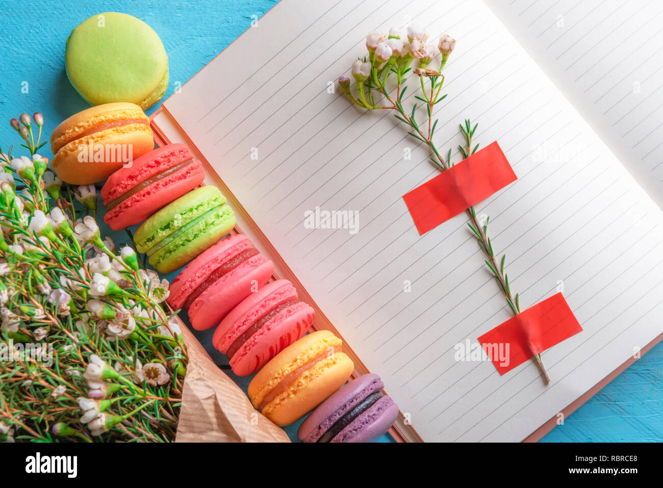 Aprire il notebook con fiore bloccato su di esso, multicolore amaretti e minuscoli fiori bianchi bouquet. Al di sopra di vista del francese dessert e fiori di primavera. Donne d Foto Stock