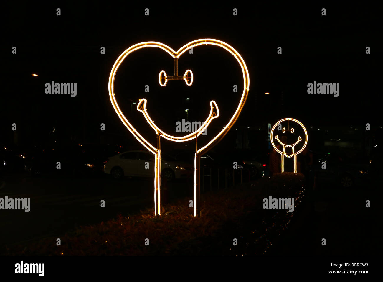 A forma di cuore faccia sorridente neon insegna luminosa sul lato della strada di notte Foto Stock