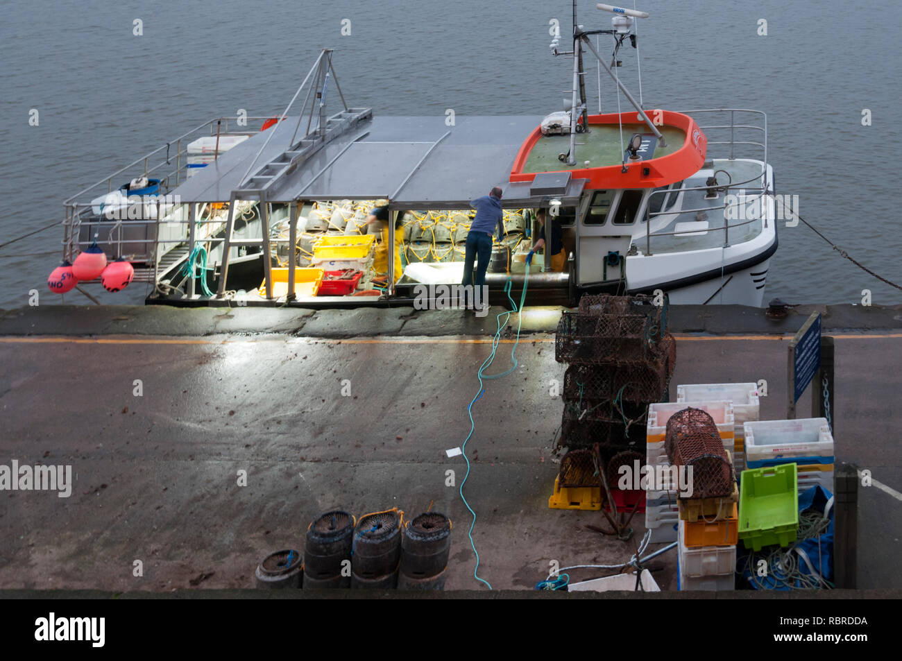 Il caricamento di una barca da pesca con pentole di granchio al tramonto a Wells quay sulla Costa North Norfolk Foto Stock
