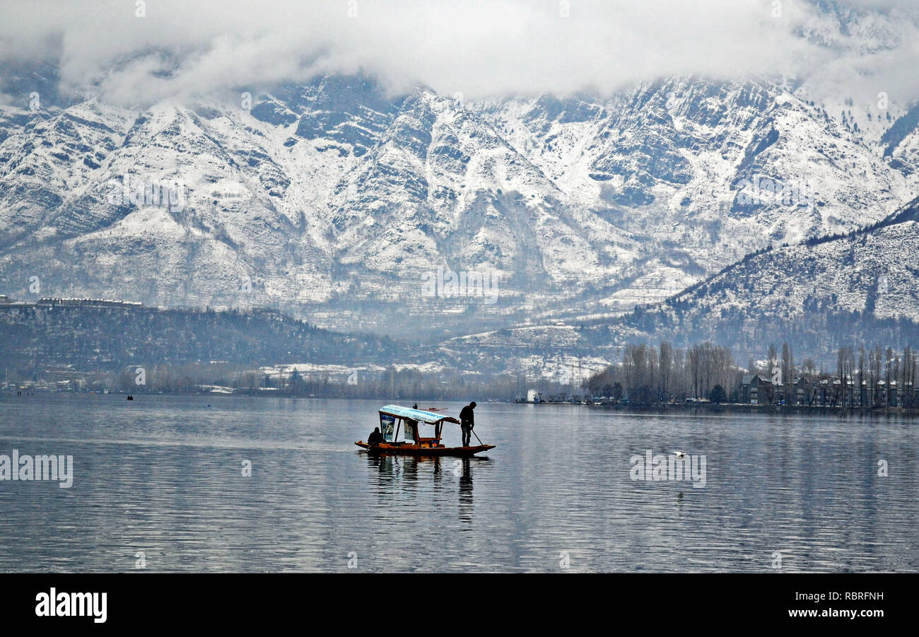 Una Shikara visto attraversando la Dal lago con lo sfondo di montagne coperte di neve dopo la nevicata fresca a Srinagar, Indiano Kashmir amministrato. La questione del Kashmir, comprese le pianure della valle, ricevuto nevicata fresca giovedì notte che ha continuato fino a venerdì mattina. Il Met Office ha previsto la luce intermittente delle precipitazioni per le prossime 24 ore. Foto Stock