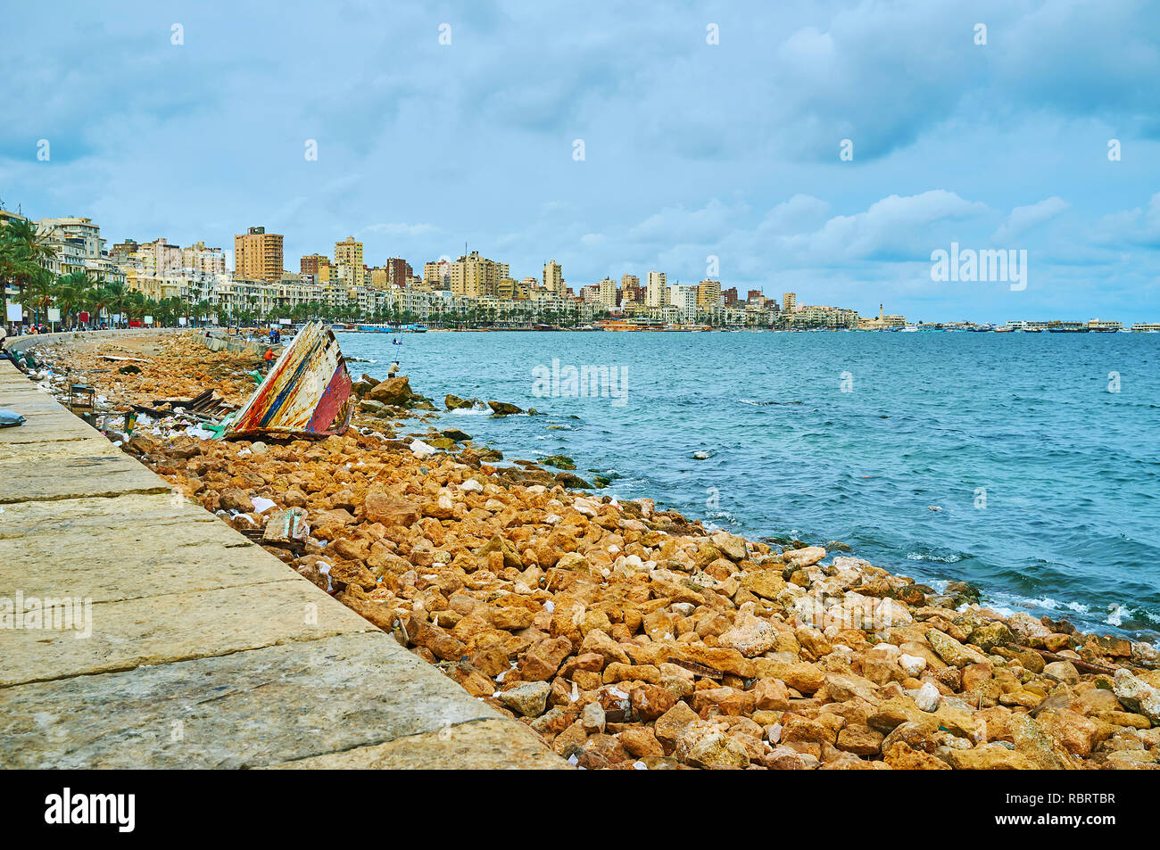 Vecchia barca relitto sulla riva di pietra di Alessandria con una vista sulla città urbana quartieri su sfondo, Egitto. Foto Stock