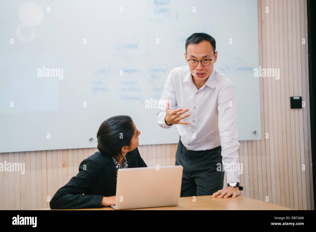 Un variegato team aziende hanno un incontro dibattito intorno a un computer portatile in ufficio. Un uomo cinese e donna indiana parla intensamente l'uno con l'altro. Foto Stock