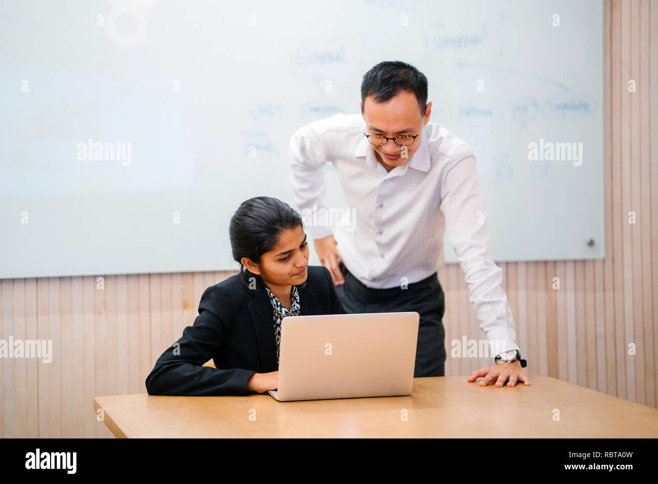 Un professore cinese o un insegnante ha una discussione con il suo studente indiano. Sono dirigere la loro attenzione a un computer portatile per la riunione. Foto Stock