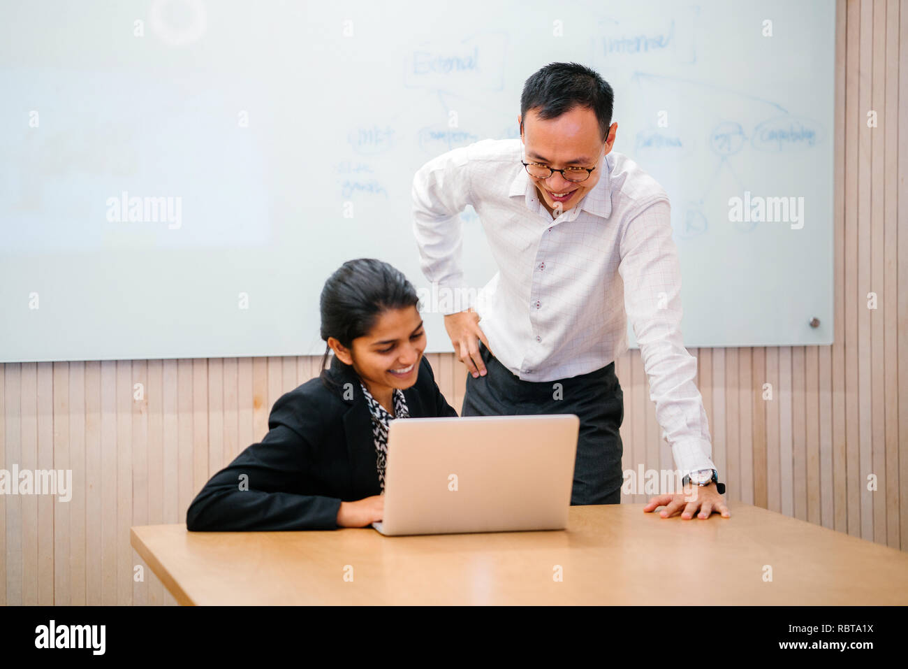 Un variegato team aziende hanno un incontro dibattito intorno a un computer portatile in ufficio. Un uomo cinese e donna indiana parla intensamente l'uno con l'altro. Foto Stock