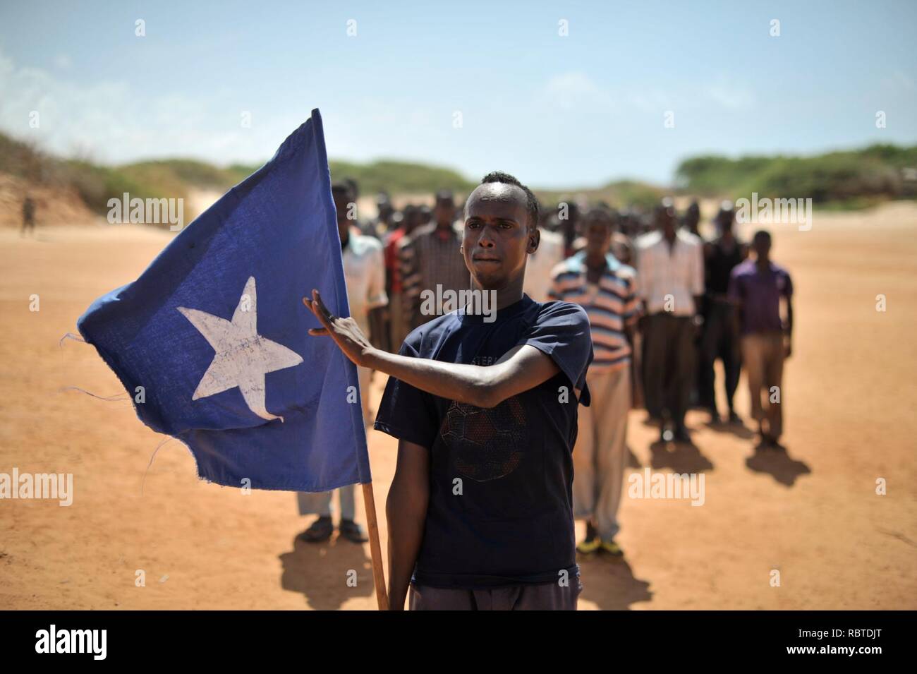 Un giovane uomo porta la bandiera somala mentre il leader di un gruppo di soldati durante una dimostrazione di una milizia locale, formata in modo da fornire la sicurezza nella città di Marka, Somalia, il 30 aprile. AU ONU (14077872251). Foto Stock